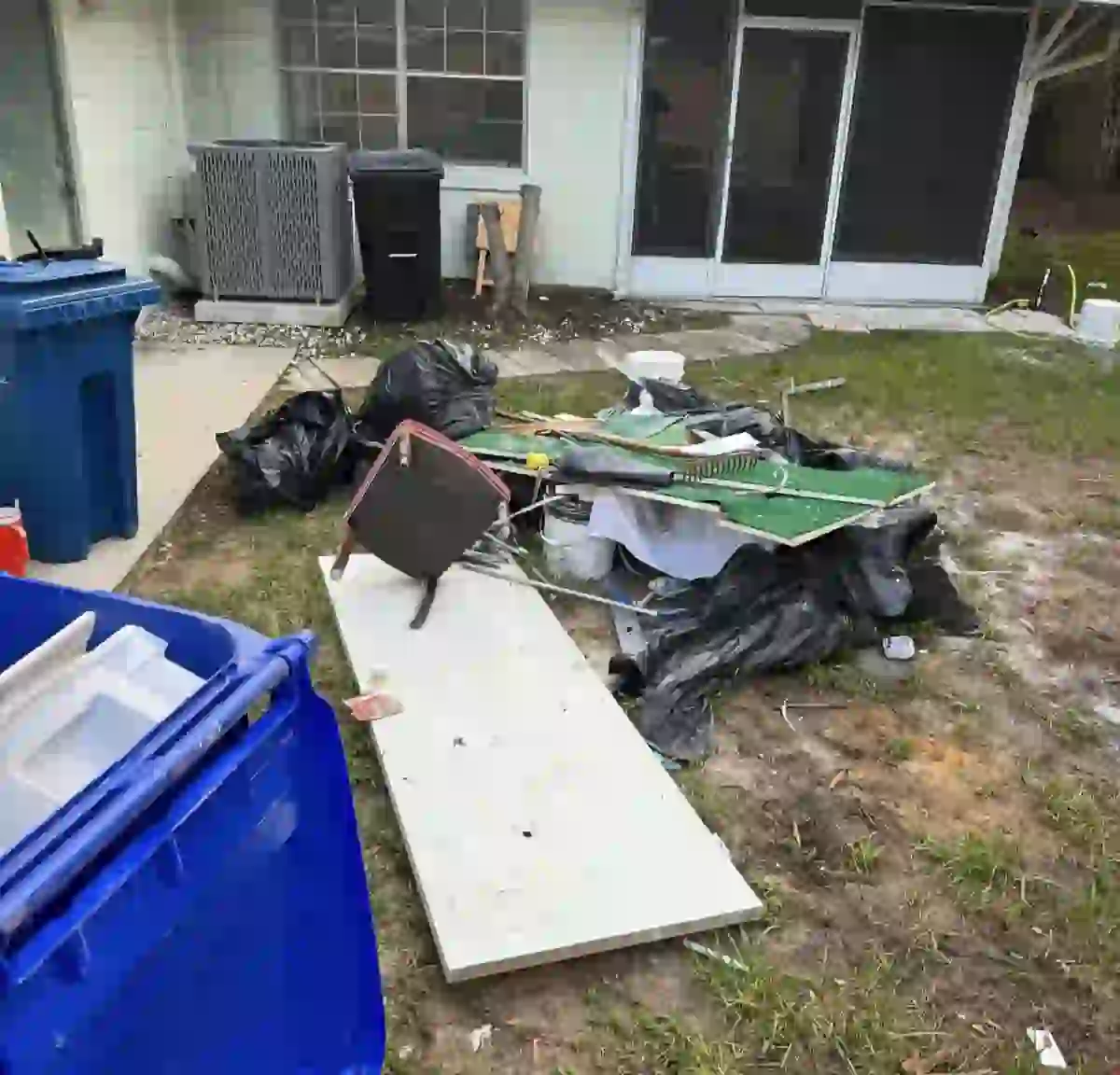 Backyard before: pile of trash bags, broken furniture, boards and yard debris